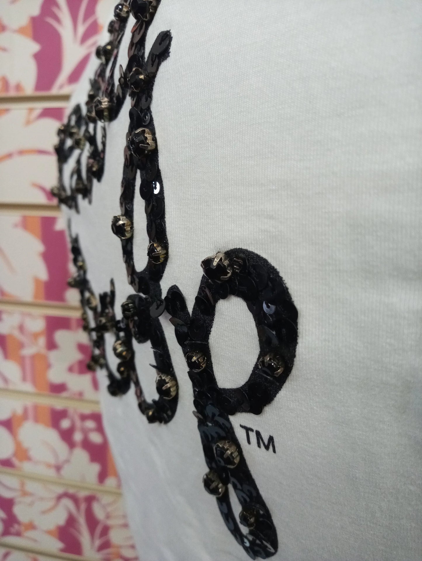 Dettaglio t-shirt bianca streetwear con scritta ricamata in paillettes nere, stile urban moda donna