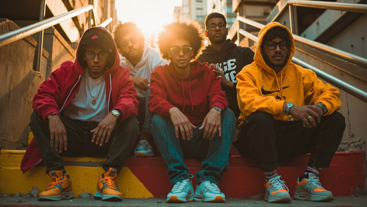 Giovani con felpe colorate streetwear, jeans e sneakers, stile urban su scale all'aperto al tramonto.