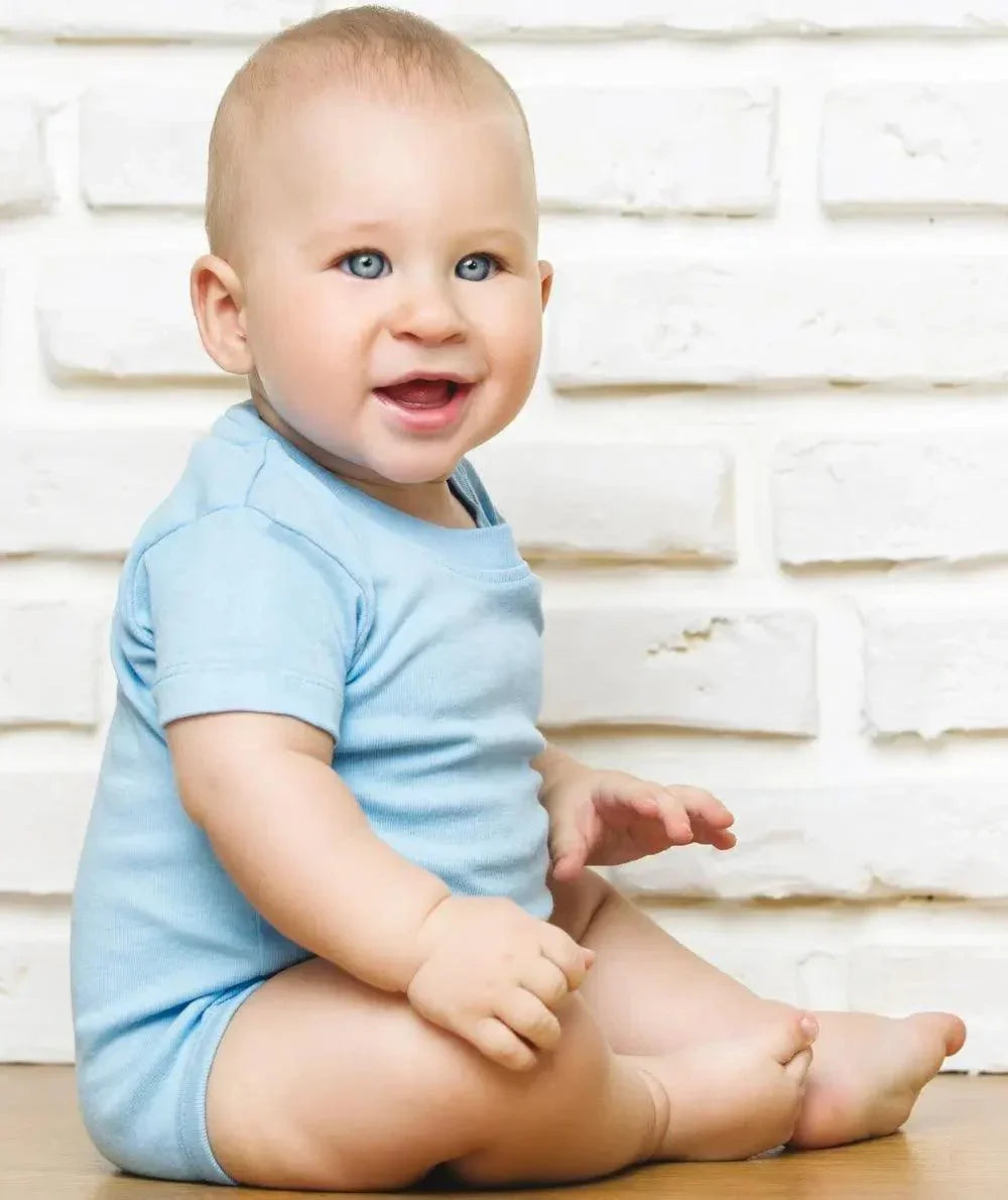 Bambino sorridente con body azzurro in cotone, stile streetwear, muro bianco sullo sfondo