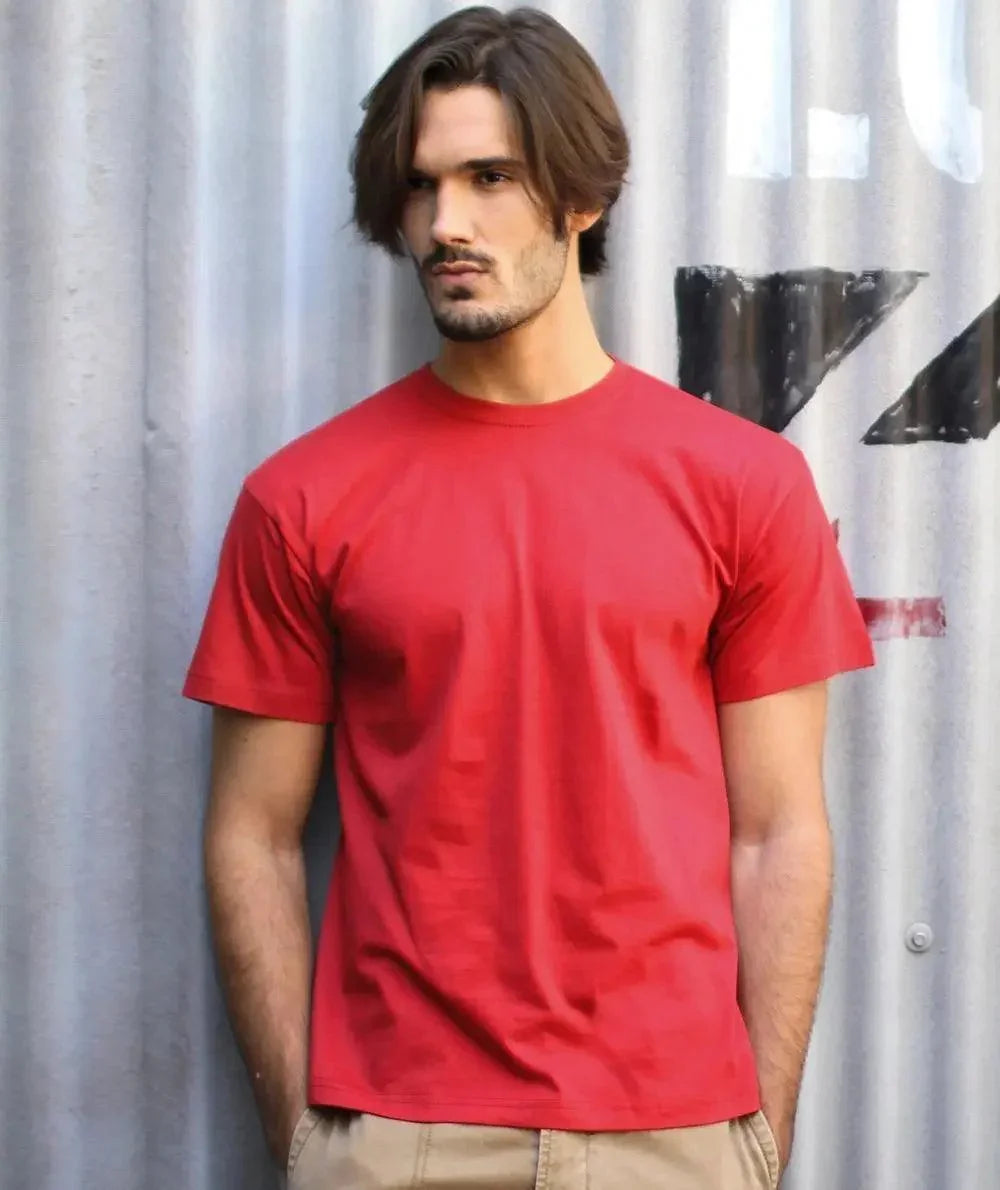 Uomo street style con t-shirt rossa e pantaloni beige davanti a muro industriale, moda urban