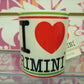 Tazza mug bianca con scritta I love Rimini, stile streetwear, su sfondo decorato colorato.