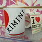 Tazza mug bianca con stampa I Love Rimini, stile street style, su sfondo floreale rosa