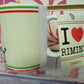 Tazza mug bianca con scritta I love Rimini, stile streetwear, esposta su sfondo colorato