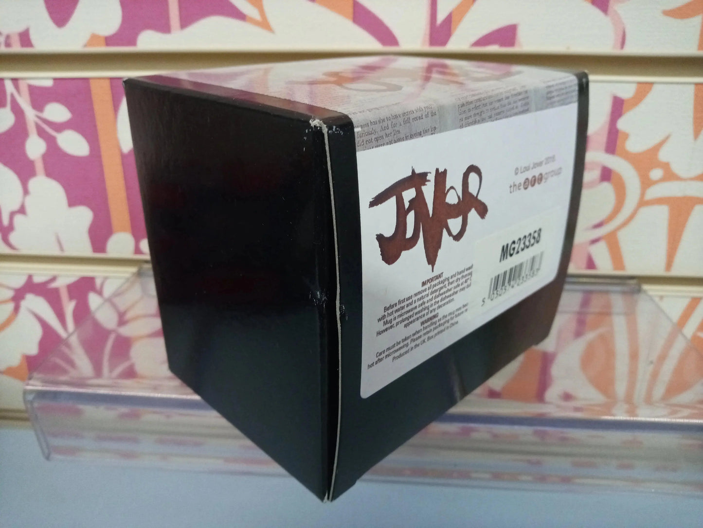 Scatola nera con etichetta Jouer esposta su mensola, sfondo decorativo rosa e arancione