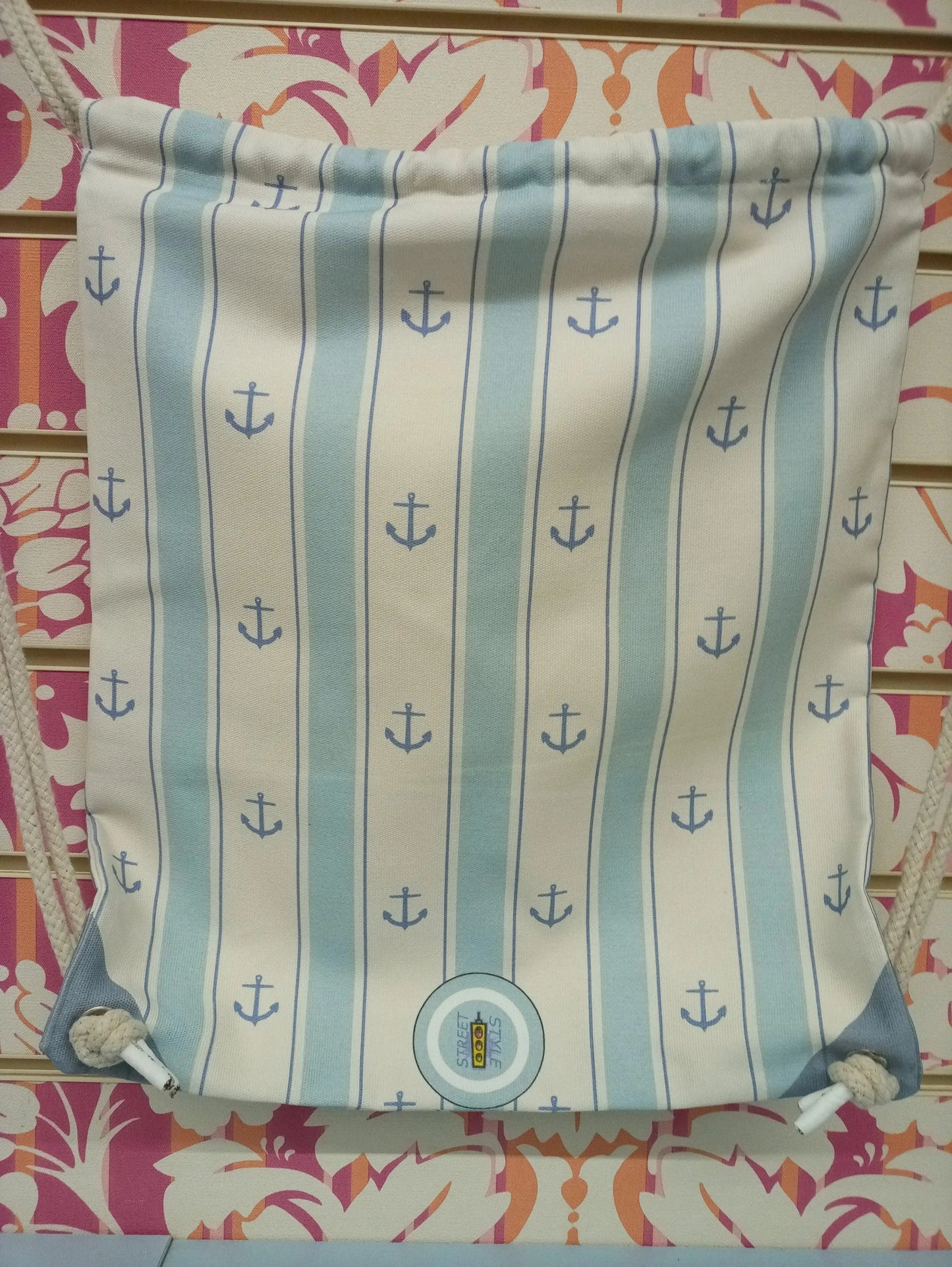 Zaino a sacca street style con righe blu e ancore, esposto su sfondo floreale colorato