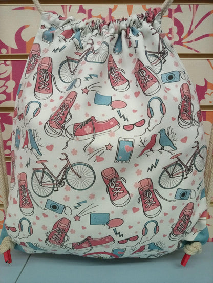 Zaino a sacca streetwear in tessuto bianco con stampe urban colorate di scarpe, bici, cuffie e dettagli rosa e azzurri.