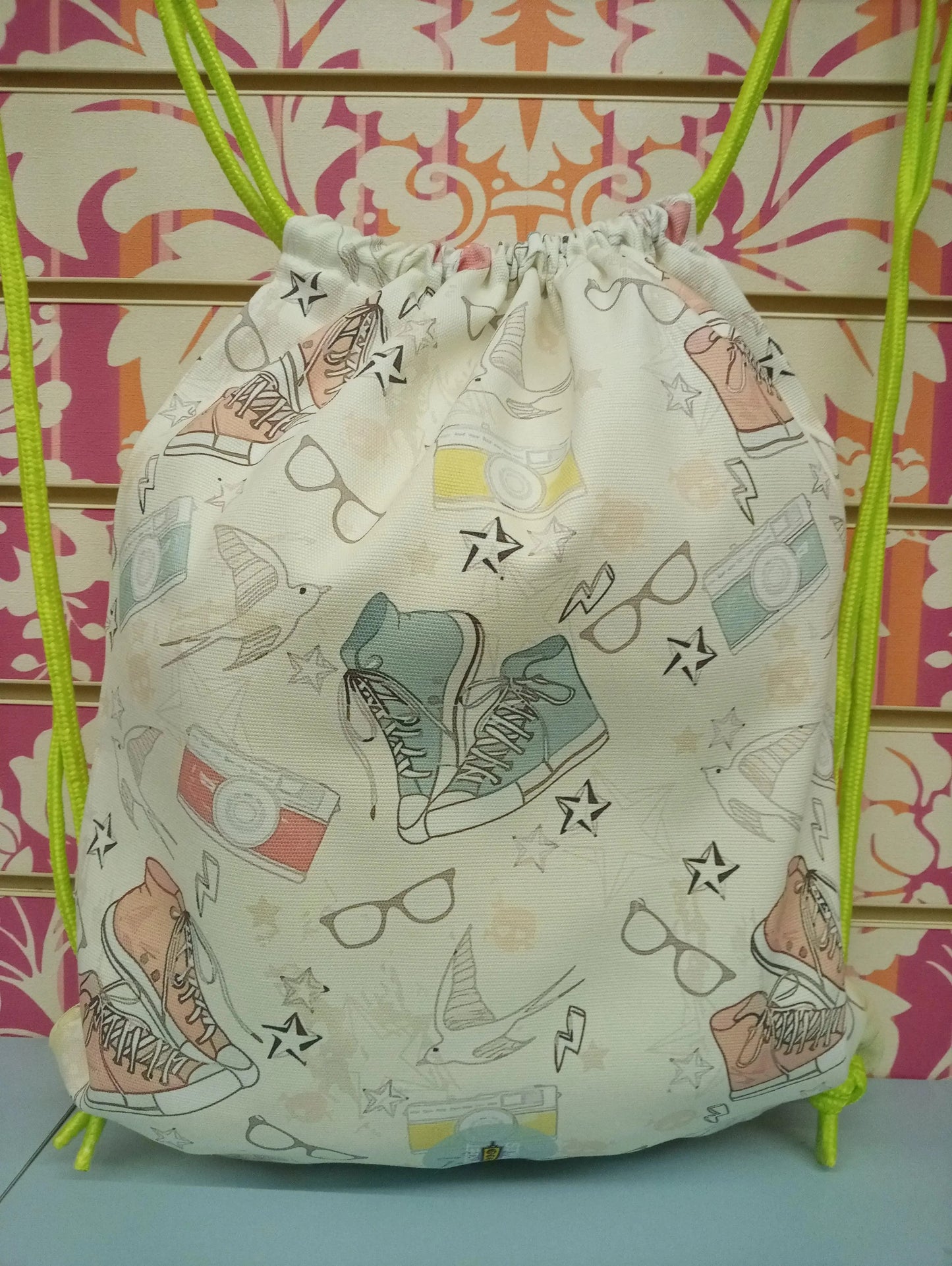 Zaino a sacca street style con disegni di sneakers, occhiali e fotocamere, cordini verdi