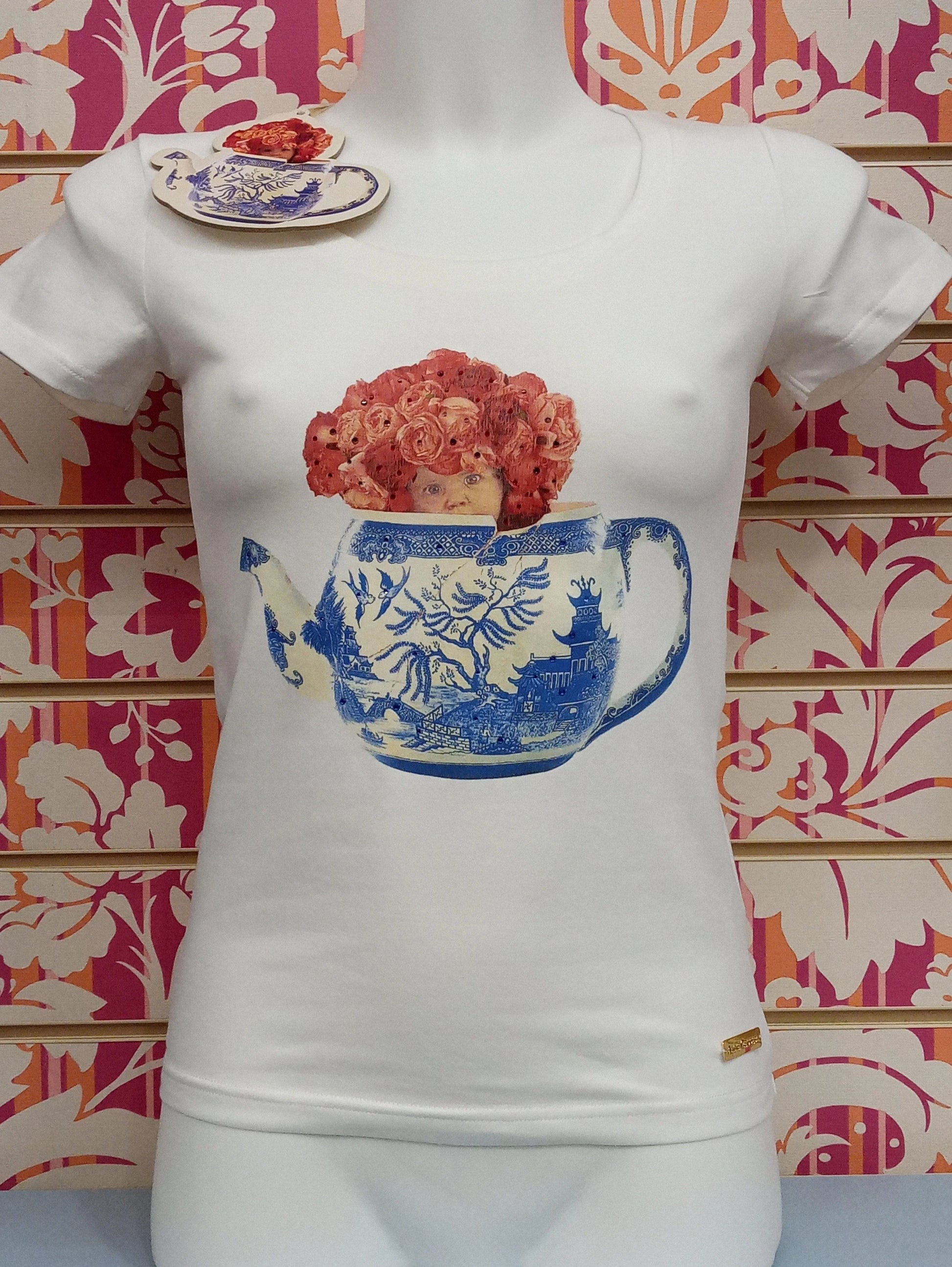 T-shirt donna bianca street style con grafica teiera blu e bambola, esposta su manichino.
